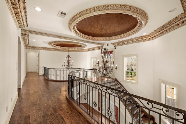 corridor with dark wood-type flooring, a notable chandelier, a towering ceiling, a tray ceiling, and ornamental molding