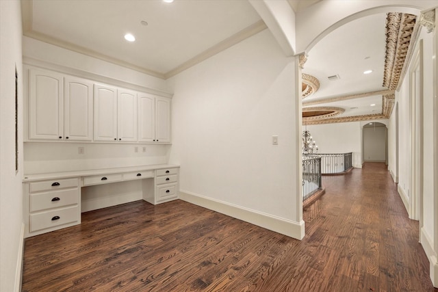 unfurnished office with dark hardwood / wood-style flooring, built in desk, and crown molding