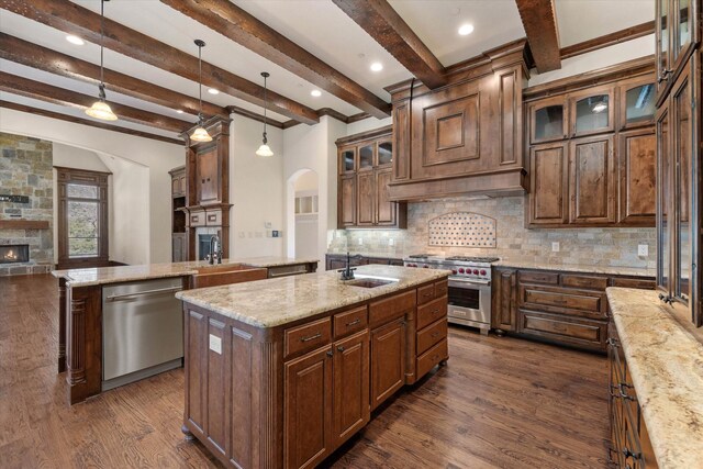 kitchen featuring beamed ceiling, decorative light fixtures, a kitchen island with sink, and stainless steel appliances