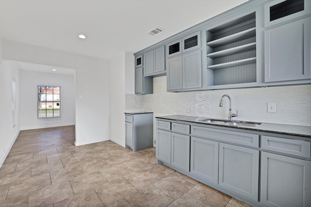 kitchen featuring decorative backsplash, gray cabinets, dark stone counters, and sink