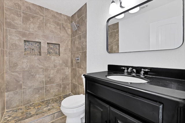 bathroom featuring a tile shower, vanity, and toilet