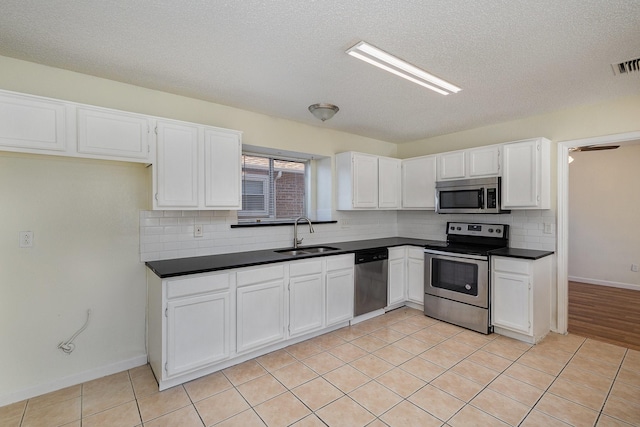 kitchen with sink, a textured ceiling, appliances with stainless steel finishes, light tile patterned flooring, and white cabinetry