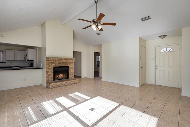 unfurnished living room with ceiling fan, beam ceiling, light tile patterned floors, high vaulted ceiling, and a fireplace