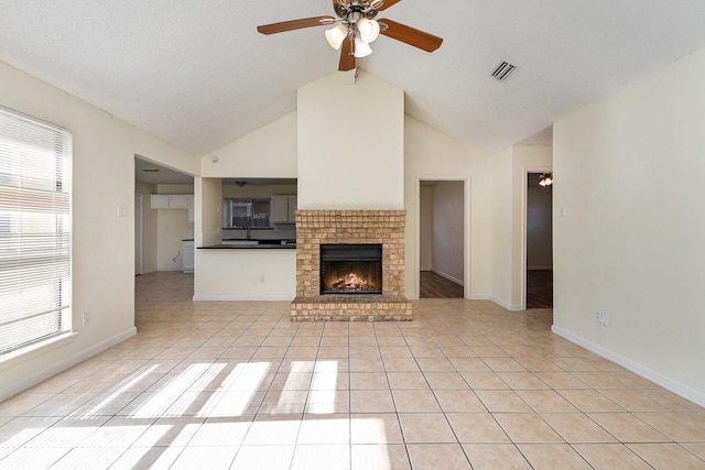 unfurnished living room featuring a fireplace, lofted ceiling with beams, ceiling fan, and light tile patterned flooring