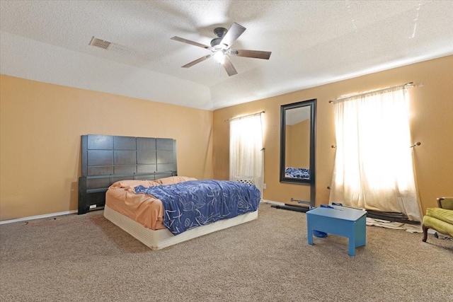 carpeted bedroom with a tray ceiling, multiple windows, ceiling fan, and a textured ceiling