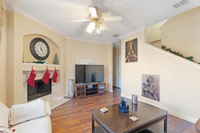 living room with a tile fireplace, ceiling fan, hardwood / wood-style floors, and ornamental molding