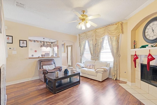 living room with crown molding, hardwood / wood-style flooring, ceiling fan, a fireplace, and a textured ceiling