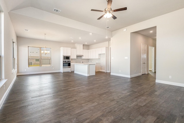 unfurnished living room with ceiling fan with notable chandelier and dark wood-type flooring