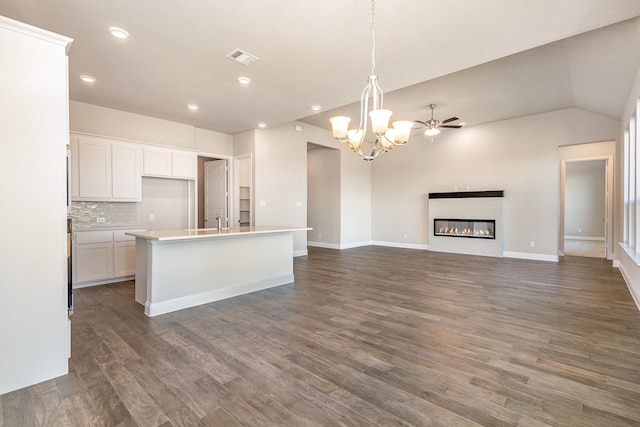 kitchen with decorative backsplash, ceiling fan with notable chandelier, a kitchen island with sink, pendant lighting, and white cabinetry