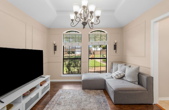 living area with an inviting chandelier, a raised ceiling, and dark wood-type flooring