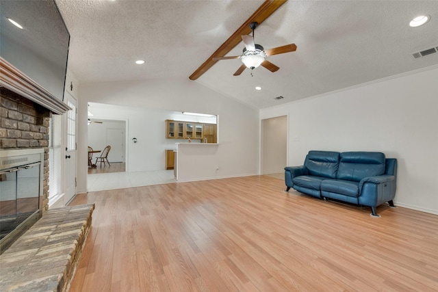 living area featuring light wood-type flooring, a textured ceiling, ceiling fan, lofted ceiling with beams, and a fireplace