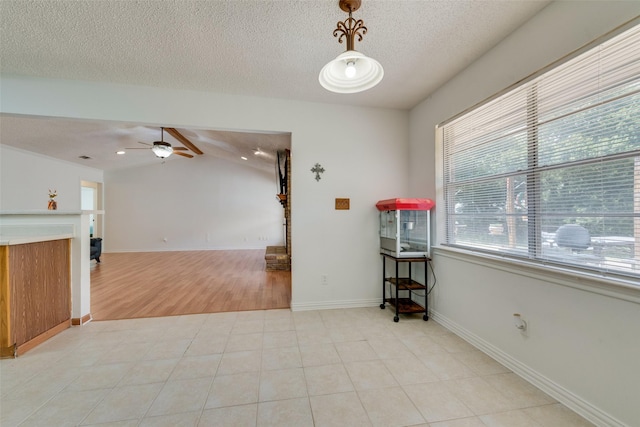 tiled empty room featuring vaulted ceiling with beams, ceiling fan, a textured ceiling, and a brick fireplace