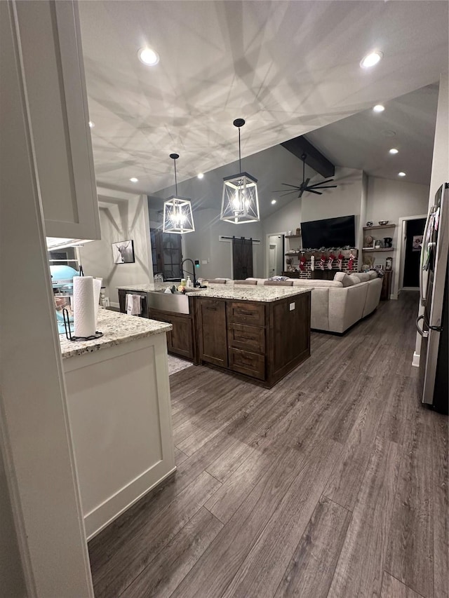 kitchen featuring light stone counters, ceiling fan, pendant lighting, a center island, and stainless steel refrigerator