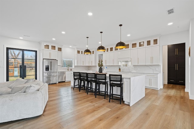 kitchen with stainless steel appliances, decorative light fixtures, a kitchen island with sink, a breakfast bar, and white cabinets