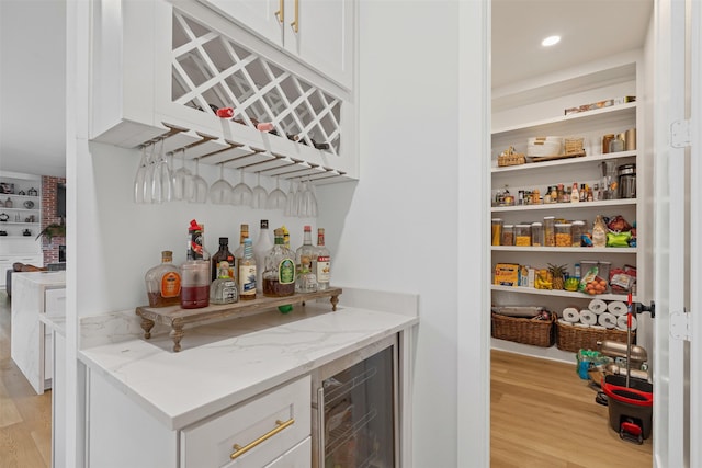 bar featuring light stone countertops, light wood-type flooring, white cabinets, and wine cooler