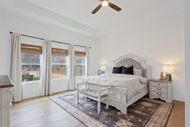 bedroom with a tray ceiling, ceiling fan, and light hardwood / wood-style floors