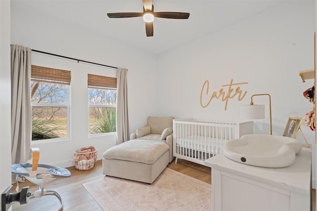 bedroom featuring ceiling fan, light hardwood / wood-style floors, and a crib