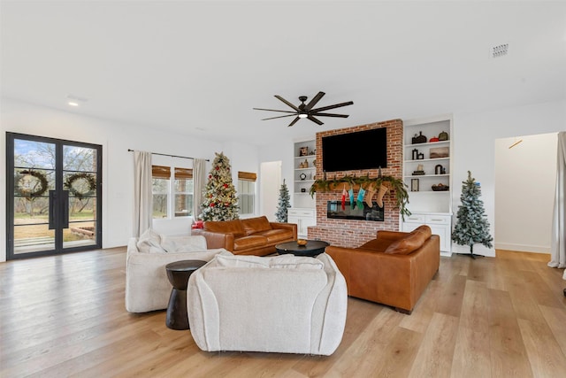 living room featuring a brick fireplace, light wood-type flooring, built in features, and ceiling fan