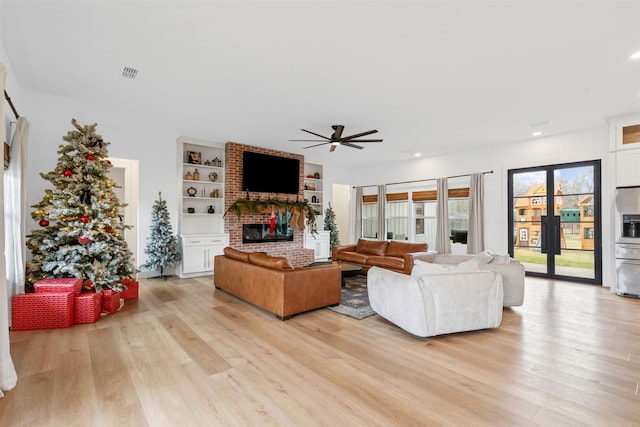 living room featuring a fireplace, ceiling fan, light hardwood / wood-style flooring, and built in shelves