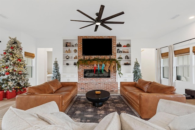 living room with built in features, wood-type flooring, a brick fireplace, and ceiling fan