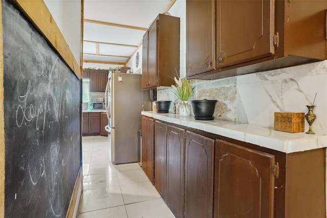 kitchen with tasteful backsplash, stainless steel refrigerator, dark brown cabinets, and light tile patterned floors