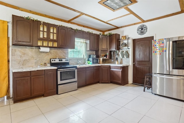 kitchen with tasteful backsplash, dark brown cabinets, light tile patterned floors, and stainless steel appliances