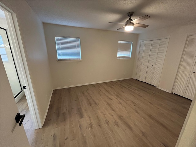 unfurnished bedroom featuring a textured ceiling, two closets, light hardwood / wood-style flooring, and ceiling fan