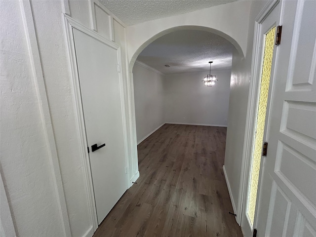 hallway featuring a textured ceiling, dark hardwood / wood-style floors, an inviting chandelier, and crown molding