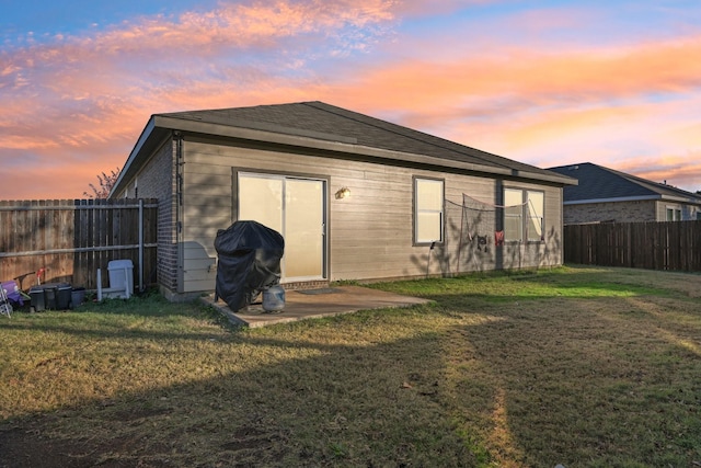 back house at dusk featuring a lawn