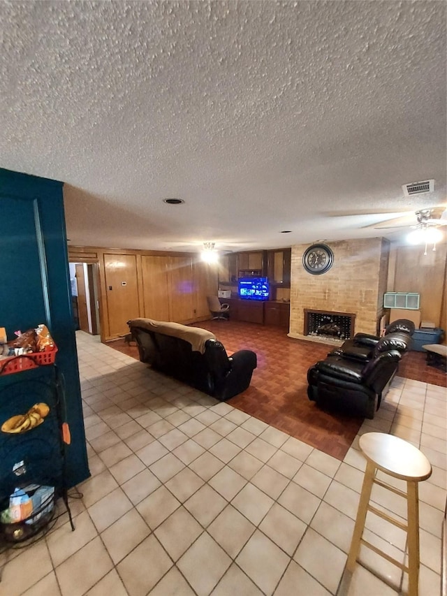 tiled living room featuring a tiled fireplace, wood walls, and a textured ceiling