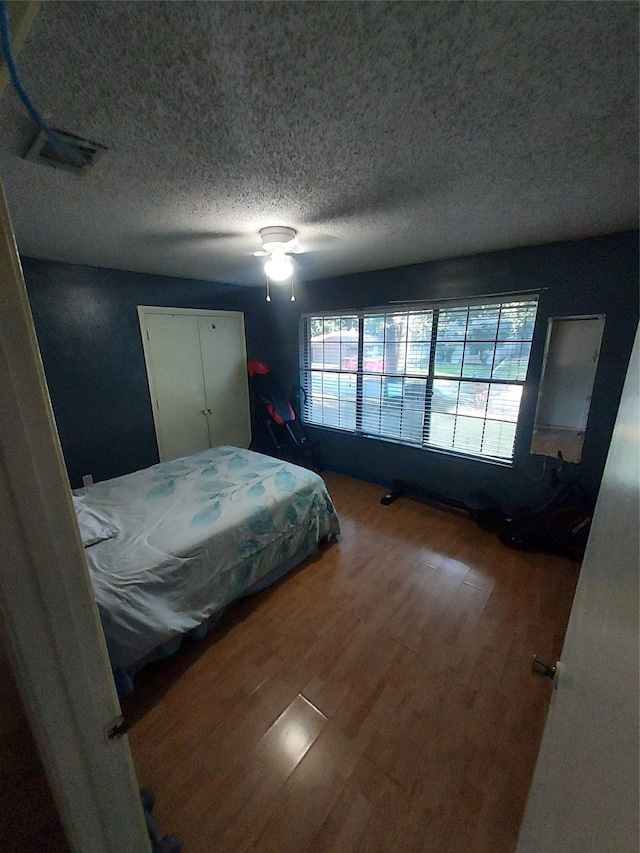 bedroom with ceiling fan, wood-type flooring, and a textured ceiling