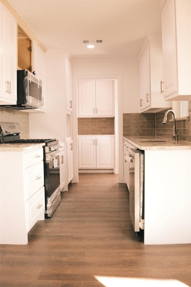 kitchen featuring dark wood-type flooring, white cabinets, backsplash, and appliances with stainless steel finishes