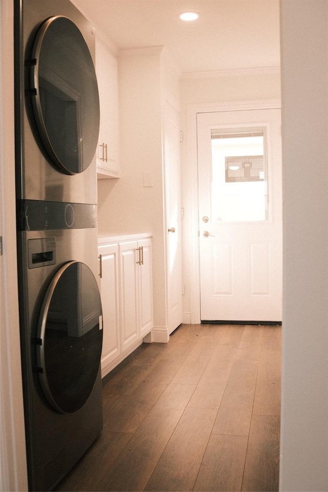 clothes washing area with cabinets, crown molding, and stacked washer and dryer