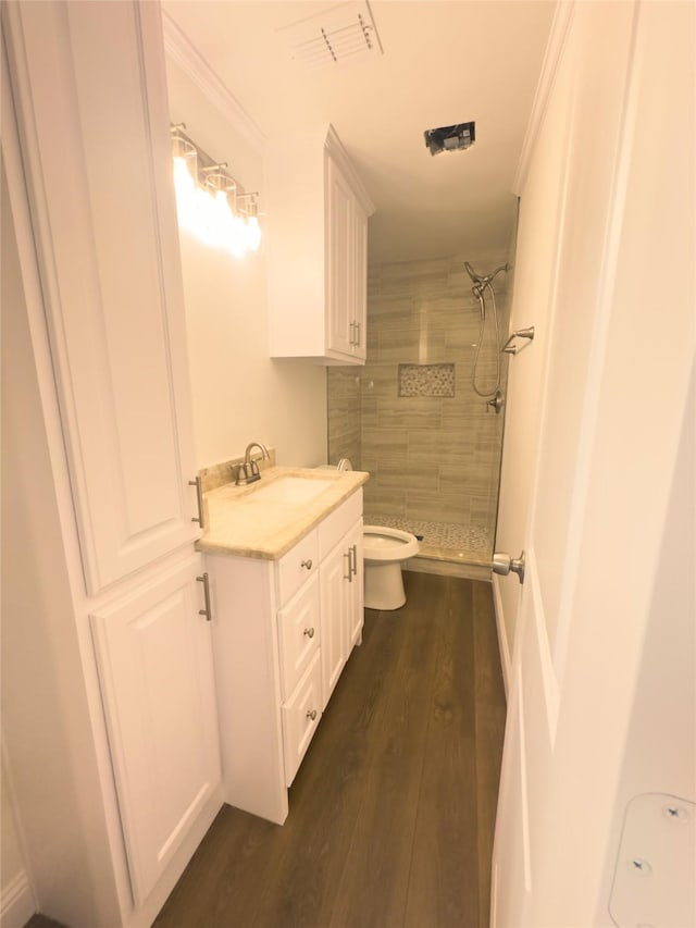 bathroom with hardwood / wood-style floors, vanity, toilet, ornamental molding, and tiled shower