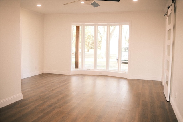 unfurnished room featuring ceiling fan, a barn door, ornamental molding, and dark hardwood / wood-style floors