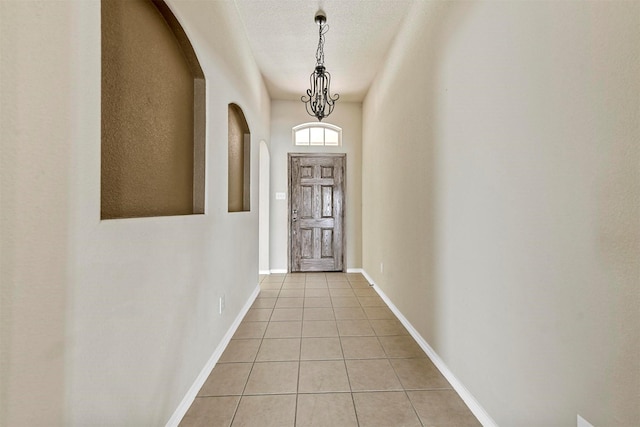 doorway to outside with light tile patterned flooring, a textured ceiling, and an inviting chandelier