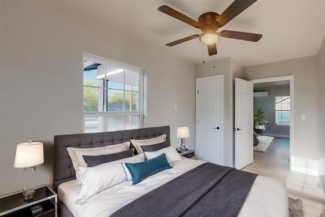 bedroom with ceiling fan, light wood-type flooring, multiple windows, and an AC wall unit