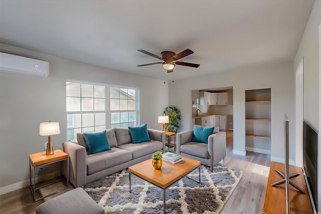 living room with sink, light hardwood / wood-style flooring, built in shelves, ceiling fan, and a wall mounted AC