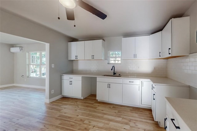 kitchen featuring an AC wall unit, sink, white cabinets, decorative backsplash, and light wood-type flooring