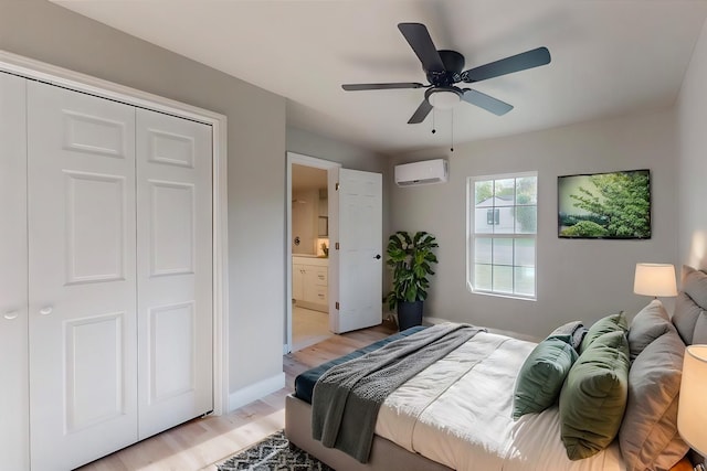 bedroom featuring ceiling fan, ensuite bath, a wall unit AC, and light hardwood / wood-style flooring