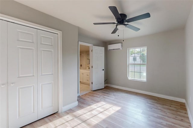 unfurnished bedroom featuring ensuite bathroom, a wall mounted air conditioner, a closet, and light hardwood / wood-style flooring