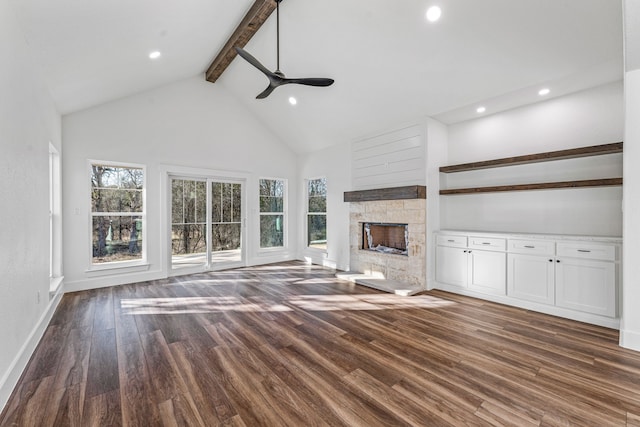 unfurnished living room featuring a stone fireplace, high vaulted ceiling, dark hardwood / wood-style floors, beamed ceiling, and ceiling fan