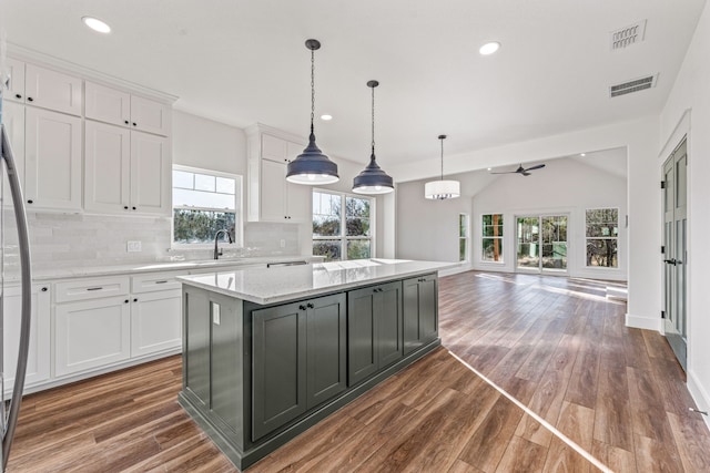 kitchen with light stone counters, decorative light fixtures, a kitchen island, decorative backsplash, and white cabinets