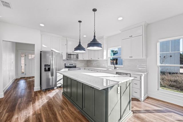 kitchen with a kitchen island, decorative light fixtures, white cabinetry, light stone counters, and stainless steel appliances