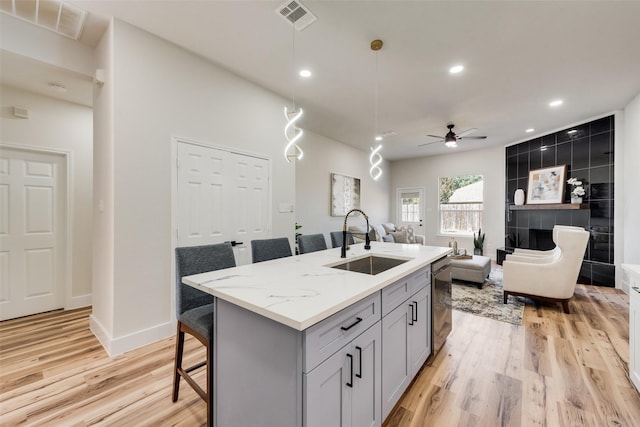 kitchen with a kitchen bar, sink, gray cabinets, an island with sink, and light stone countertops