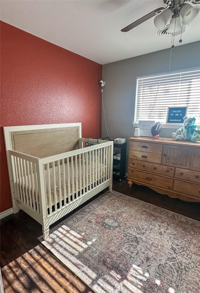 unfurnished bedroom with ceiling fan, a nursery area, a textured ceiling, and dark hardwood / wood-style flooring