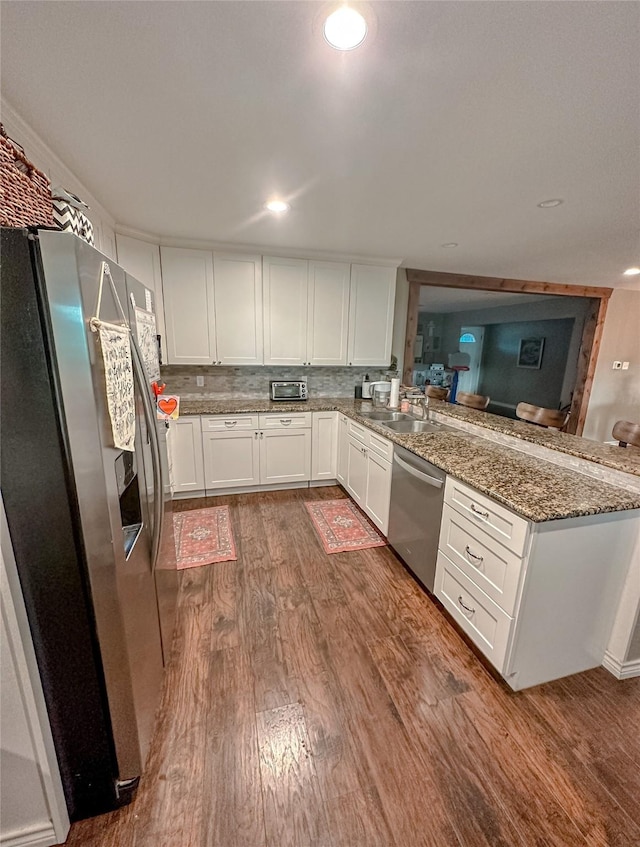 kitchen with stone counters, decorative backsplash, appliances with stainless steel finishes, dark hardwood / wood-style flooring, and white cabinetry