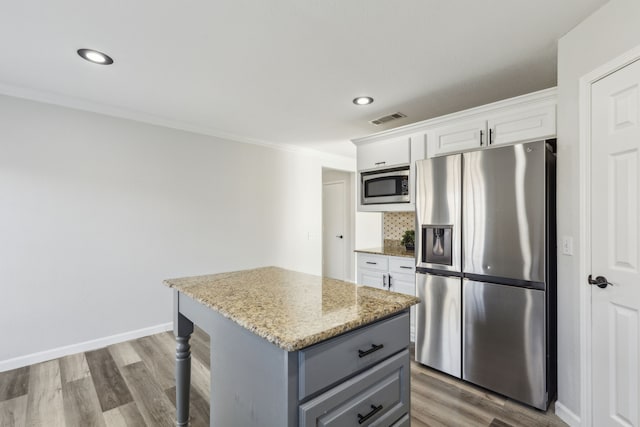 kitchen with light stone countertops, ornamental molding, stainless steel appliances, a kitchen island, and white cabinetry