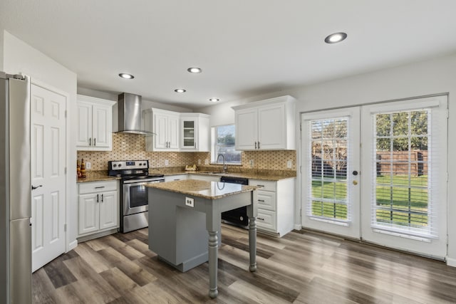 kitchen with white cabinetry, wall chimney exhaust hood, a kitchen breakfast bar, a kitchen island, and appliances with stainless steel finishes