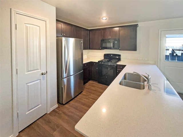 kitchen with sink, kitchen peninsula, dark brown cabinets, black appliances, and hardwood / wood-style flooring